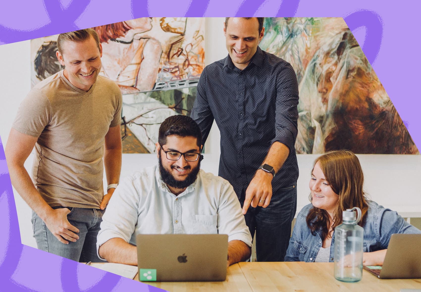 A man sitting in front of a laptop at work with three co-workers looking over his shoulder