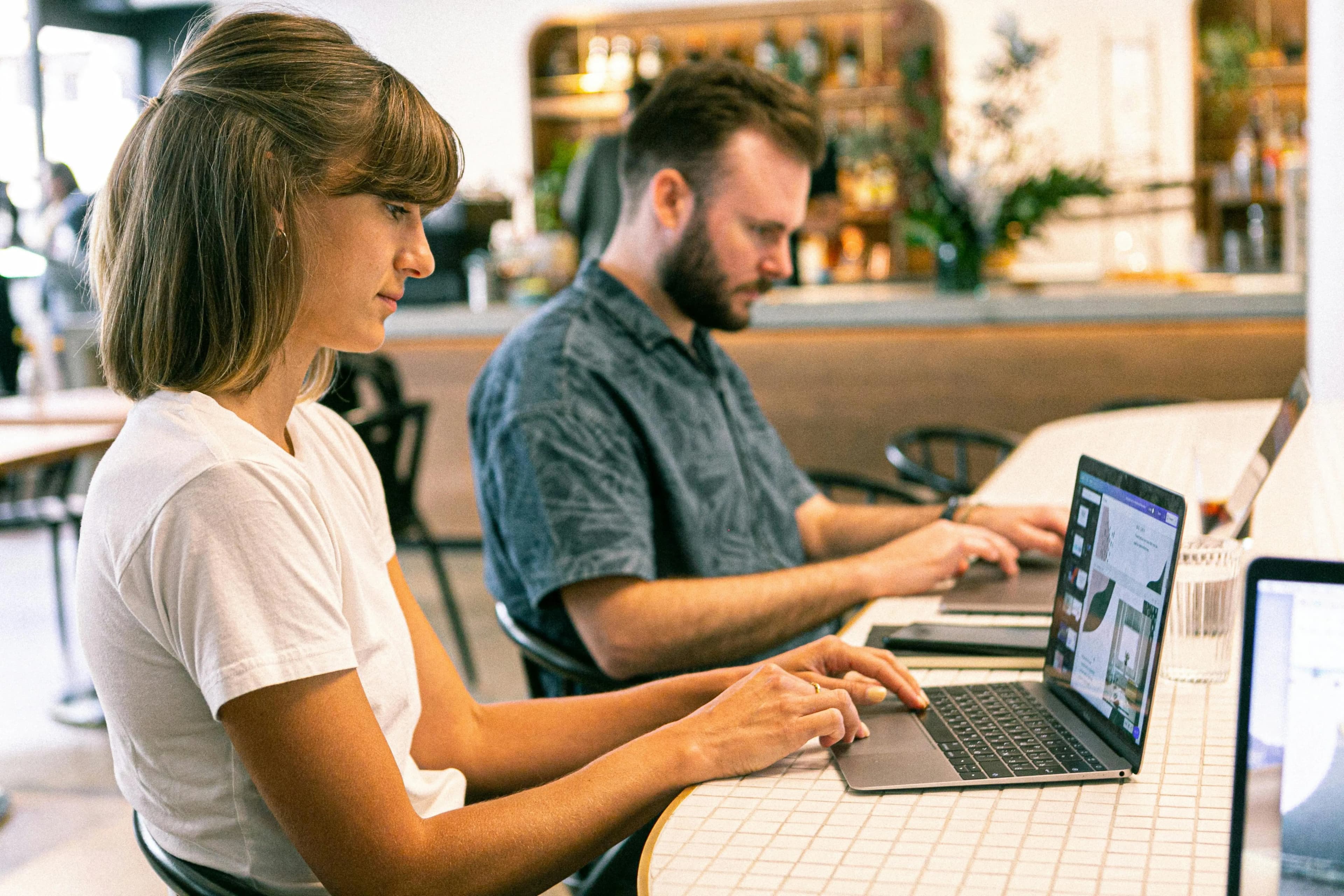 A woman and male sitting at a work desk together, both working on their laptops.
