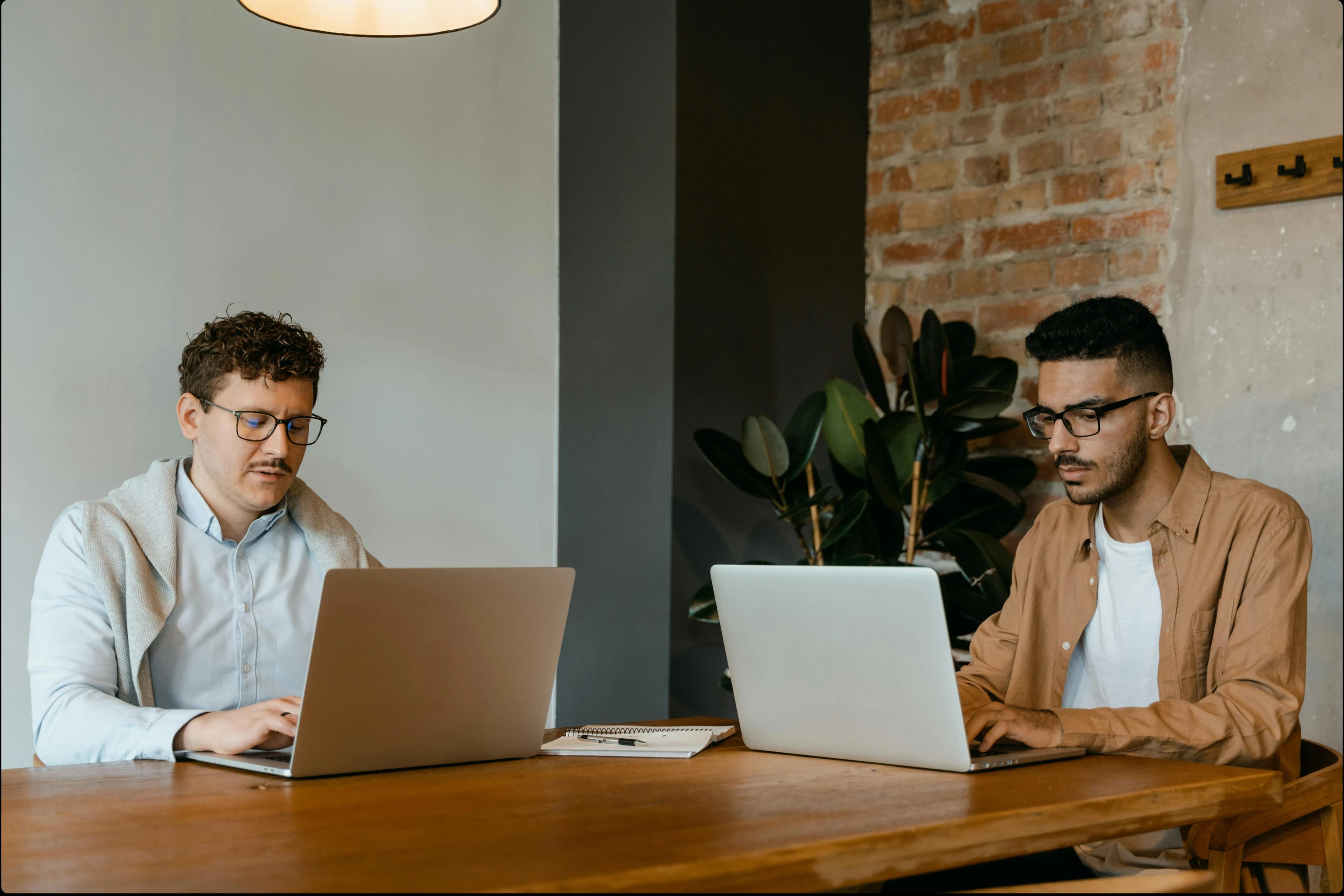 Two men working on their laptops on the same table.
