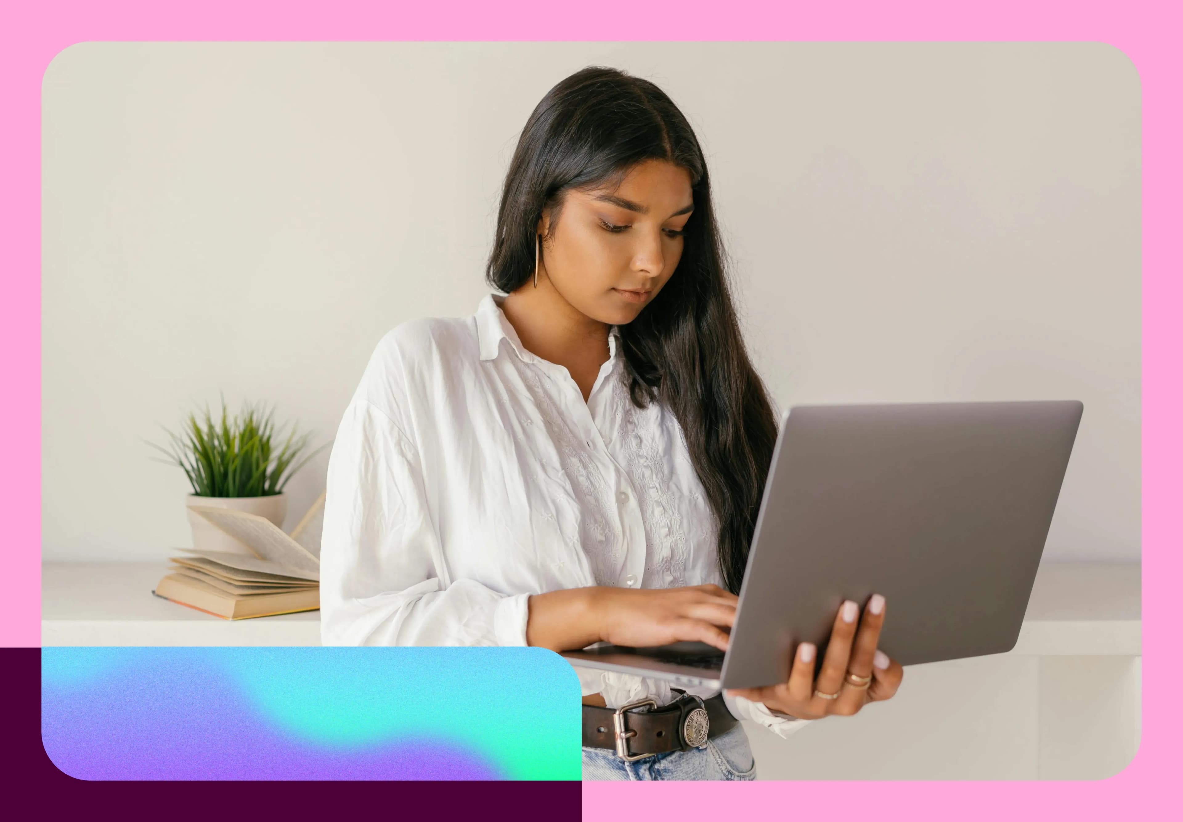 Woman in a white blouse using a laptop, standing near a desk with a plant and books. The image has a colorful border.